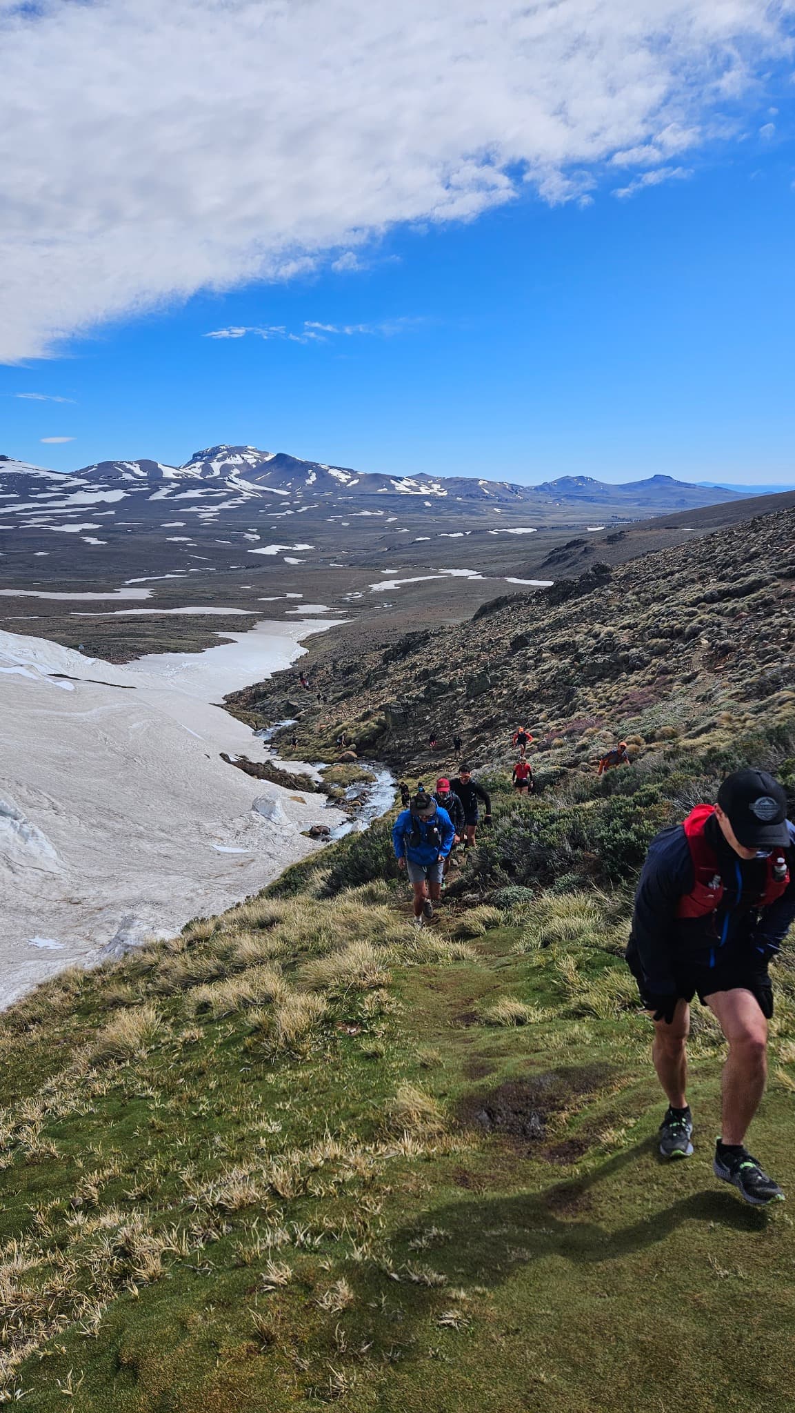 Grupo de trail running subiendo un cerro nevado con su entrenador